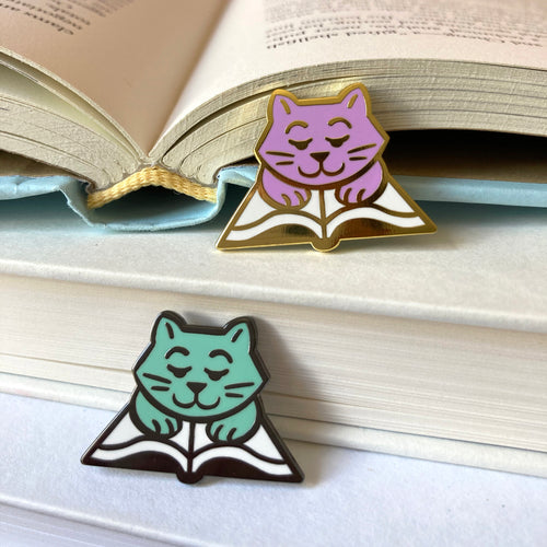 Bookstore cats as enamel pins drawn as a cartoon style cat reading a book