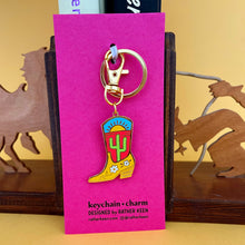 The cowgirl Cactus Boot keychain shown on its pink display card