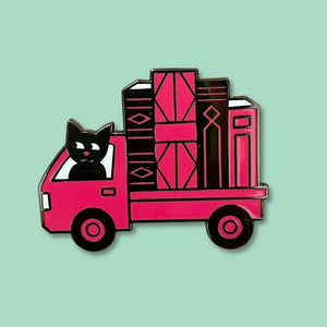 The Book Truck enamel pin by Rather Keen. This black and red enamel pin is shaped like a Japanese kei truck loaded with giant books and driven by a cute cat.