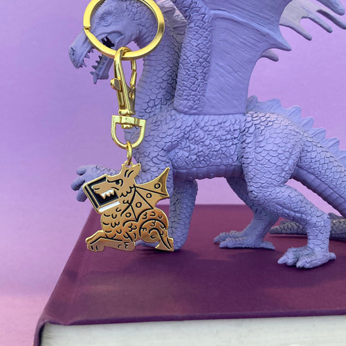 Book Dragon keychain by Rather Keen - a metallic gold dragon shape keychain held by a purple dragon toy.