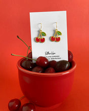 Cherry earrings by Rather Keen. The gold and enamel color cherries are illustrated in a geometric style.