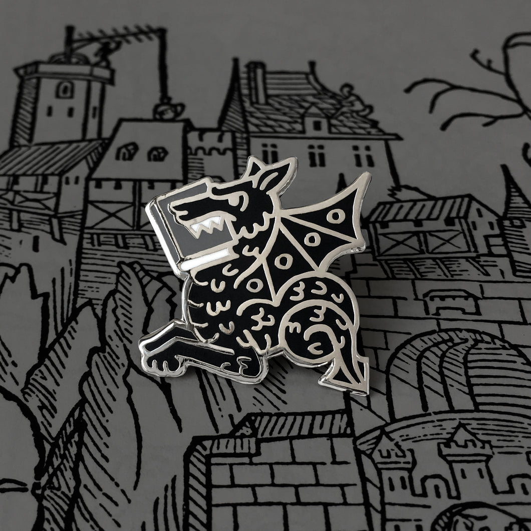 Black Book Wyrm enamel pin by Rather Keen. This pin is a medieval manuscript style dragon eating a book.