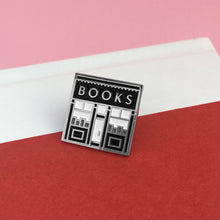 The Book Shop enamel pin photographed resting on a red book.