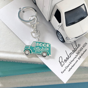 The Bookmobile keychain seen on its display card and posed with a stack of books